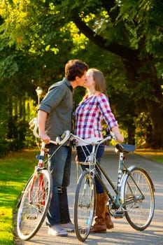 A man and a woman with their bicycles on a bike path in an outdoor park setting.