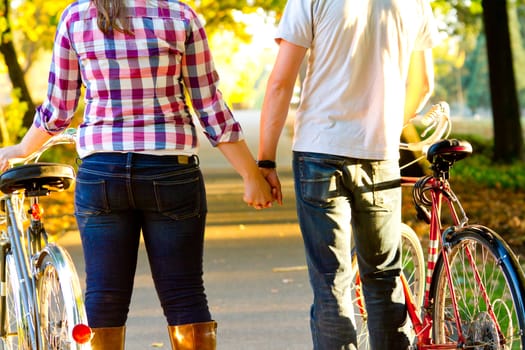 A couple takes a moment to hold hands together along a bike path with their bicycles.