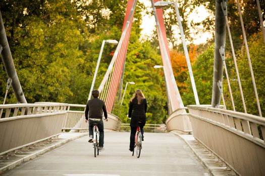 A man and woman ride their bikes together along a bike path bridge.