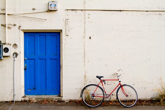 A bright blue door contrasts with this bike leaned up against the white wall.