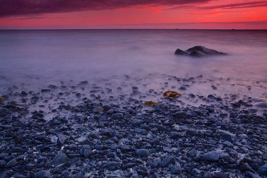 Pebble beach with red skies by sunset on Lofoten islands in Norway