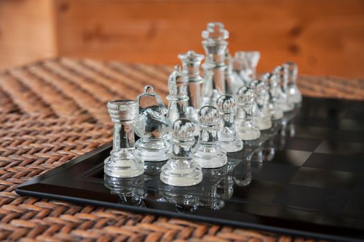 Glass chess set on a black marble board placed on a rattan table