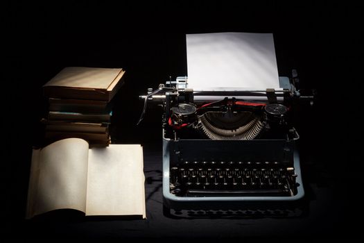 retro typewriter with stack of book and one opened book black background