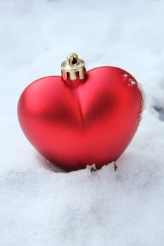 Red, heart shaped christmas ornament in fresh snow