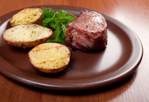 Grilled beef on white plate with potatoes salad and tomatoes  .closeup