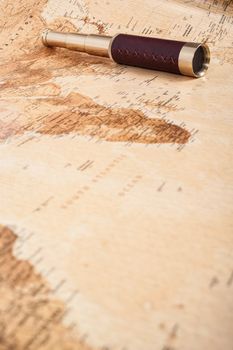 An antique, out of focus, map with a beautiful golden and leather telescope.