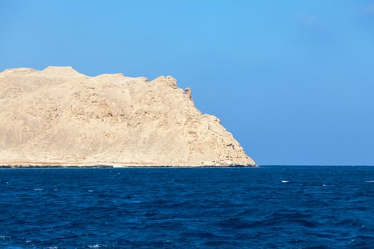 Wavy sea with stony bare mountain in the background under a clear blue sky