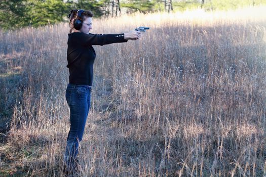 Woman with protective hearing and eye wear shooting a revolver.