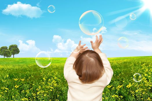 The small girl plays with soap bubbles. Nature
