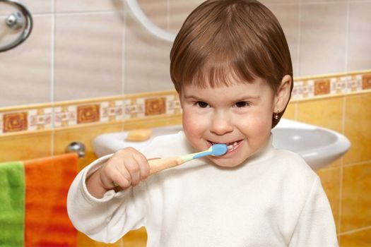 The small girl cleans teeth in a yellow bathroom