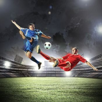 two football players in jump to strike the ball at the stadium