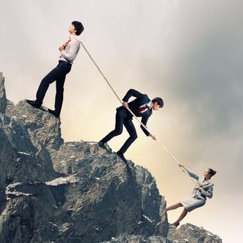 Image of three businesspeople pulling rope atop of mountain