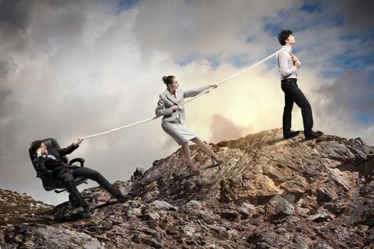 Image of three businesspeople pulling rope atop of mountain