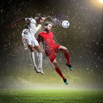 two football players in jump to strike the ball at the stadium