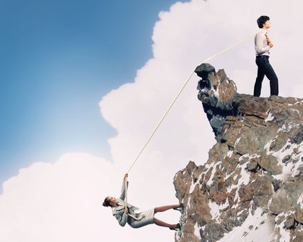 Image of busionessman and businesswoman pulling rope atop of mountain