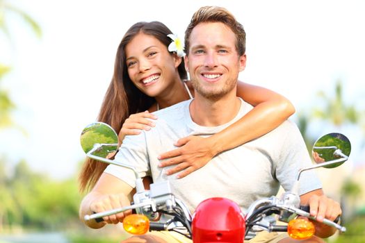Happy young couple in love on scooter driving together. Multiracial couple having fun in the free outdoor. Smiling Caucasian man and Asian woman.