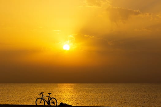 bicycle silhouette on the beach, golden sky at the sunrise sea background