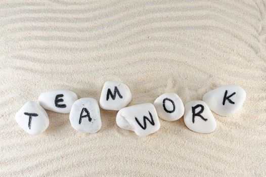 Teamwork word on group of stones with sand background