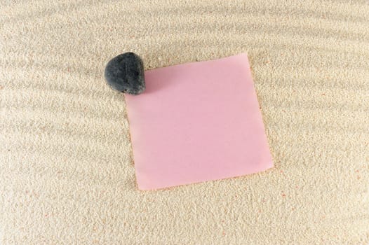 Blank paper on the sand with a stone on it