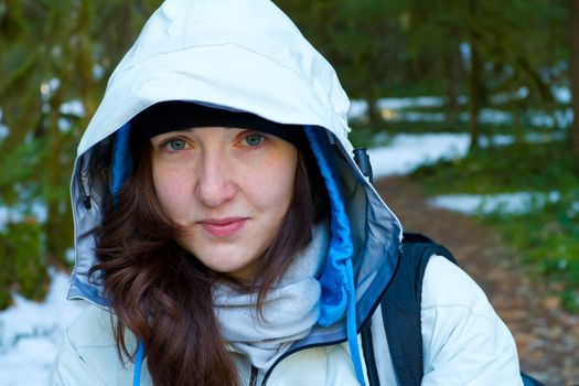 A woman pauses during her hike for a rest and to look at the camera while wearing a white jacket.