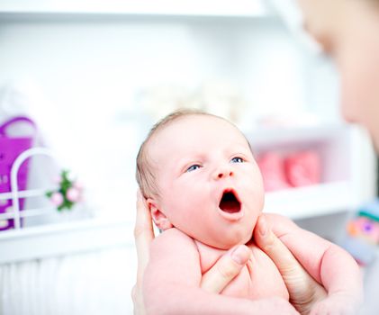 Cute yawning tiny baby being held in its mothers hands as she prepares to dress it in the nursery, closeup of the infants face