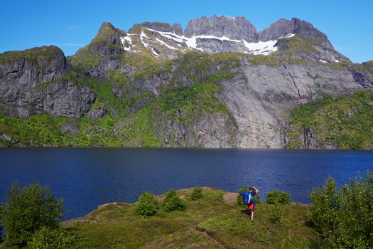 Young hiker with backpack standing by fjord on Lofoten islands in Norway on sunny day