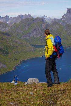 Young active hiker with backpack looking at scenic view on Lofoten islands in Norway on sunny day
