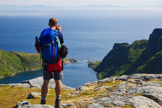 Young active man with backpack looking at scenic panorama of Lofoten islands in Norway on sunny day