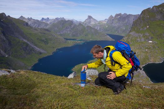 Young active man with backpack hiking on Lofoten islands in Norway on sunny day with scenic panorama in the background