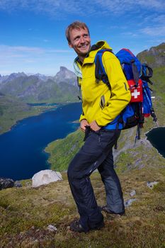 Young smiling active man with backpack hiking on picturesque Lofoten islands in Norway on sunny day