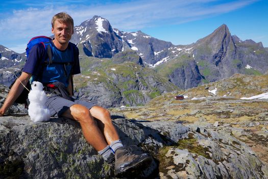 Young active man with small snowman hiking on Lofoten islands in Norway on sunny day