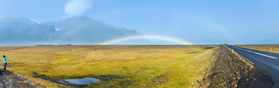 Rainbow over asphalt highway. Panorama. Iceland - famous Ring Road (Hringvegur).