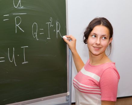 Girl in physics class writing formulas on a blackboard