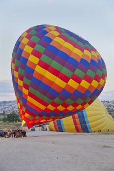 Hot air balloons being readied for rides before day break and roadies holding them anchored. Public waiting to get into a balloon for their joy ride. Generic shot with flames shooting into the balloon but location of this image was Cappadocia Turkey