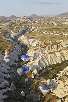 Vertical aerial landscape of hot air balloons drifting through a gorge during a low flight in Cappadocia, Turkey
