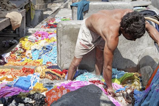 Scene at a commercial hand laundry where a workman wades through dirty laundry sorting the colors and the whites