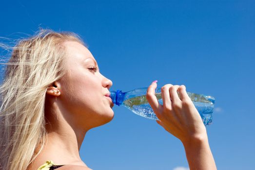 Beautiful blond girl drinking water under blue sky