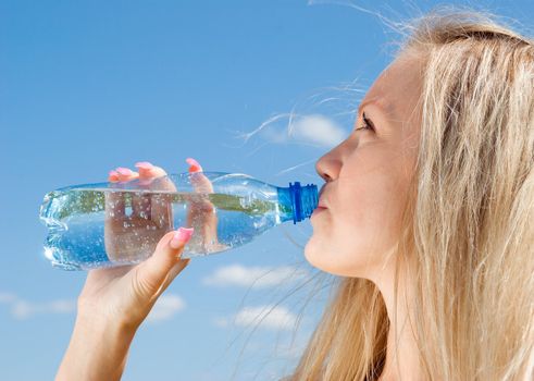 Beautiful blond girl drinking water under blue sky