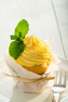 cupcake with yellow cream and fresh mint leaves as decoration on white plate