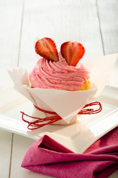 strawberry cupcake with white backing paper, red ribbon and two fresh strawberry on the top