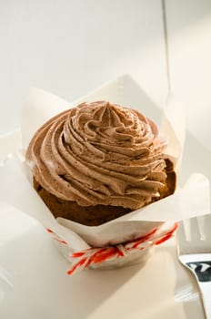 A chocolate cupcake on white plate and fork