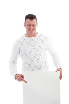 Beaming handsome young man pointing to a blank white sign which he is holding below his waist, isolated on white