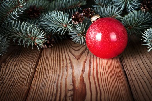 Red christmas ball on wooden background with branches of pine wood. Copy space