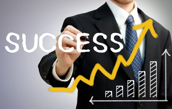 Businessman writing success with a rising arrow above a bar graph
