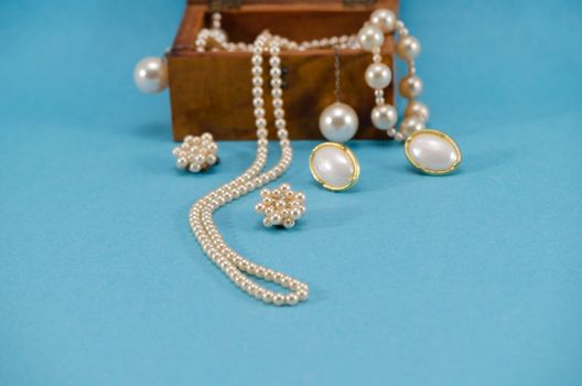 pearl jewelry beads necklace earring in retro wooden box on blue background.
