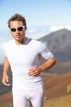 Running man. Male runner jogging outside in mountain landscape doing trail running in training for marathon race. Fit male fitness athlete in outdoor workout wearing sunglasses and compression clothes.