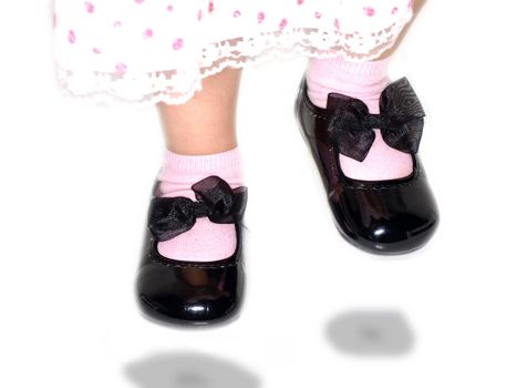Girl in cute dress, jumping high with shiny black shoes towards white