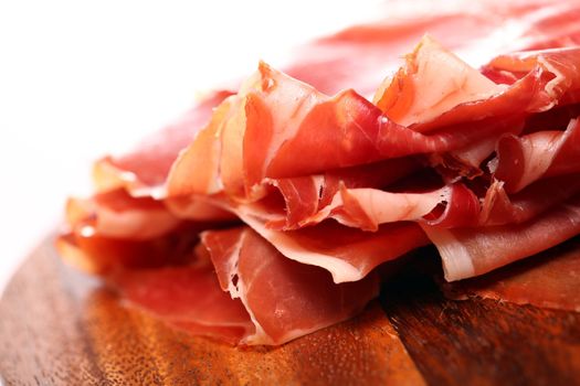 Proscuitto on a wooden plate isolated on white background