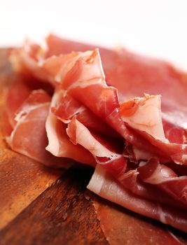 Proscuitto on a wooden plate isolated on white background