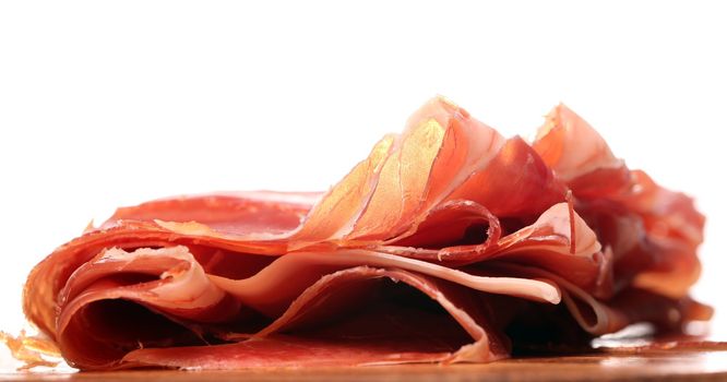 Proscuitto on a wooden plate isolated on white background